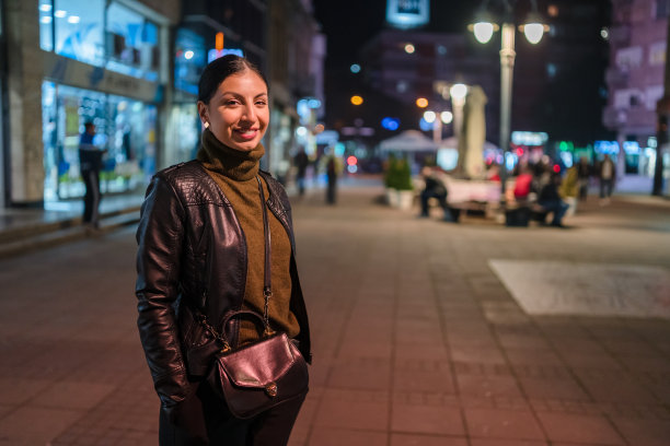 年轻女子晚上走在城市的街道上。库存图片图片下载