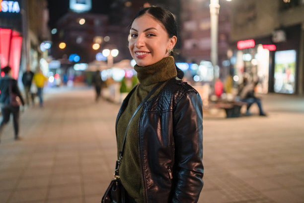 微笑的年轻女子走在夜晚的城市街道上。库存图片图片下载