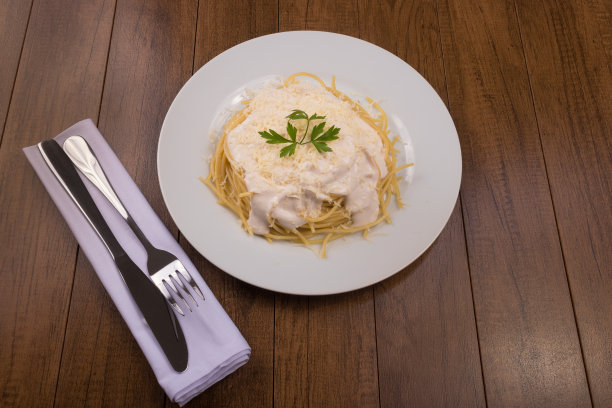意大利面配白酱，磨碎的奶酪和欧芹叶。刀叉放在白布餐巾上。集中的食物图片下载