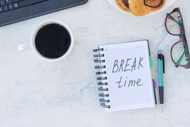 休息时间。时间概念。把单词放在工作桌上的笔记本上，用一杯咖啡和小面包打发时间图片下载