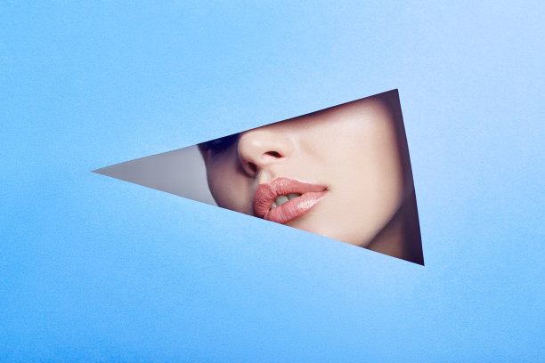 女人在看洞，明亮美丽的化妆，大眼睛和嘴唇，明亮的口红，专业化妆品和面部护理。明亮的蓝色背景和缺口插槽在纸图片下载