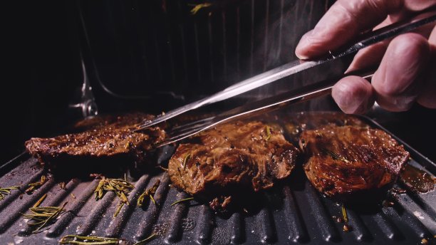 美味多汁的肉排烤制。年久半生的烤大理石牛肉。电炉，迷迭香，黑胡椒，盐。厨房钳。图片下载