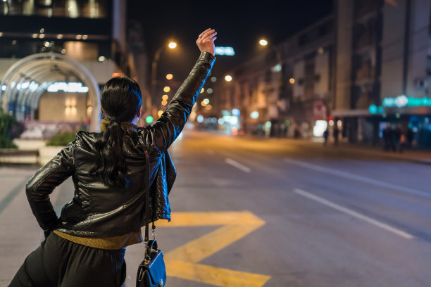一个女人站在街道上，晚上叫出租车的后视镜。库存图片图片下载