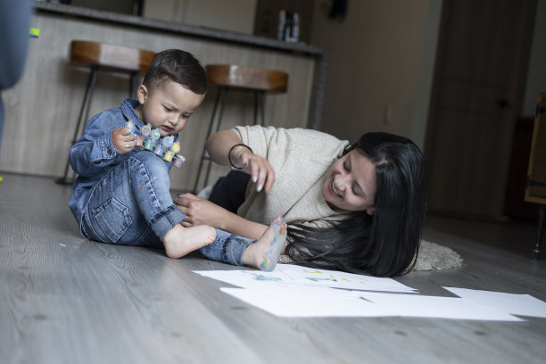 一位单身母亲和她1到2岁的孩子在客厅里玩耍的美丽时刻，她的房子的地板上放着画图片下载