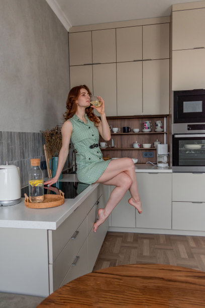 一位年轻女子坐在厨房的桌子旁，喝着装着柠檬的水。图片下载