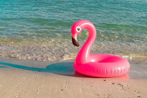 夏天的时间。粉红色的充气火烈鸟在蓝色的海水为海夏季海滩的背景。有趣的小鸟玩具的孩子。图片下载