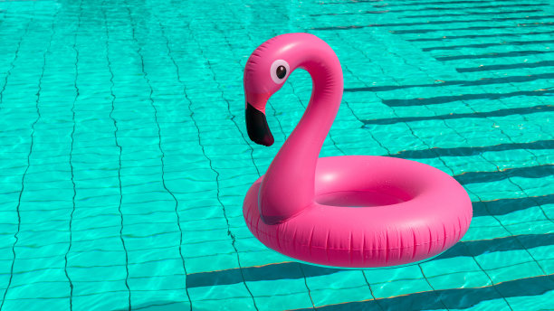 夏天有趣的海滩。粉红色的充气火烈鸟在游泳池的水为夏天的海滩背景。有趣的小鸟玩具的孩子。图片下载
