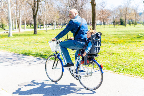 无忧无虑的爸爸和女儿在公园里骑车。慈爱的父母骑着自行车在公园里兜风，让他的孩子坐在儿童座椅上。图片下载