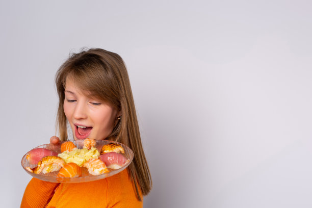 一个白人女孩拿着一盘寿司。对自制的新食谱很满意。灰色背景和边空间的文本，食谱或广告。图片下载