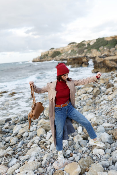 有风的秋日，在海边放松，感觉很好。户外大气的生活方式照片年轻的黑发女人的背景海。在寒冷的雨天，女人沿着灰色的暴风雨的海面走着。图片下载