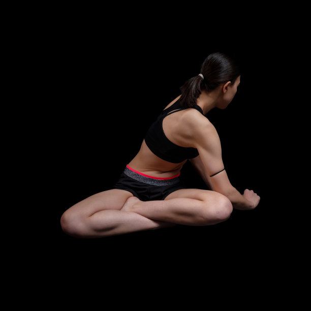 在黑色的背景下，一个年轻女子在做健身训练。图片下载