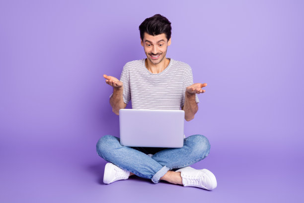 照片的家伙坐地板持有电脑牙齿微笑说话穿白色t恤牛仔裤运动鞋孤立的紫罗兰背景图片下载