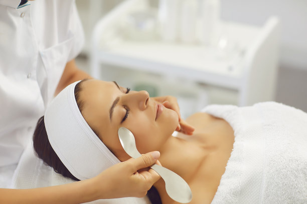 心满意足的女人闭着眼睛躺在按摩师的办公室里接受面部按摩。图片下载