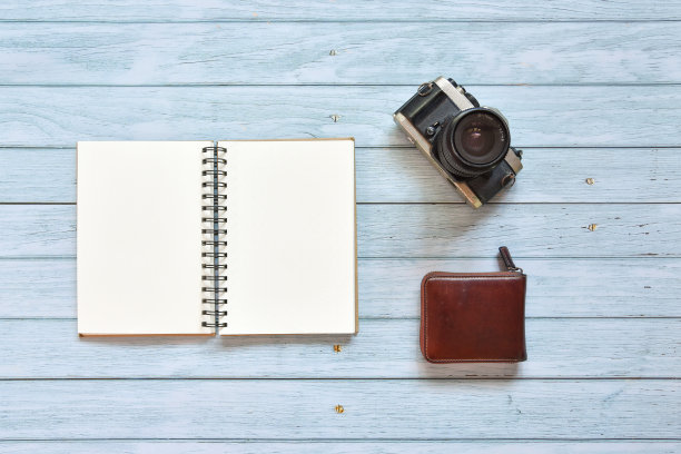 静物，商务办公室或旅行者备忘录概念，顶视图图像打开笔记本与复古电影相机和皮革钱包与空白页上的蓝天木制背景，准备添加文本图片下载