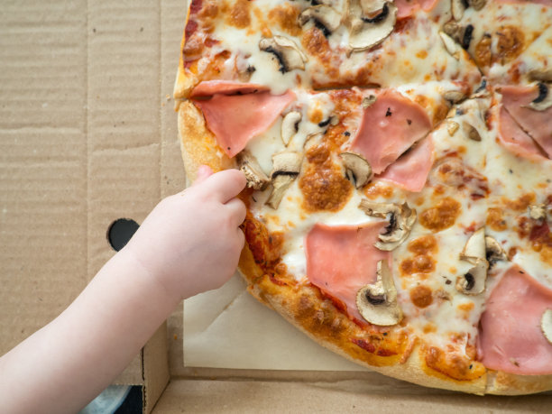 宝宝的手伸向有火腿和蘑菇的披萨图片下载