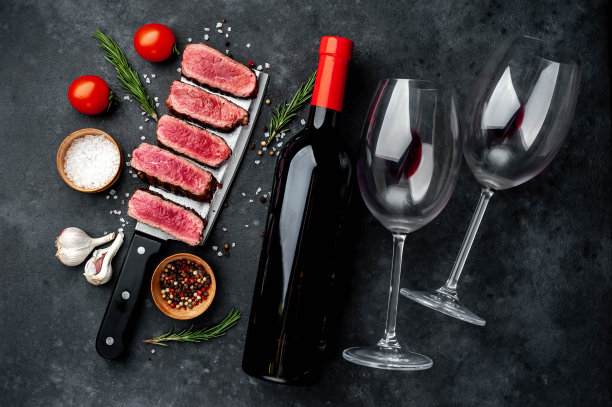 几片烤牛排放在放有香料的肉刀上，一瓶红酒和玻璃杯放在石头背景上。晚餐有两个图片下载
