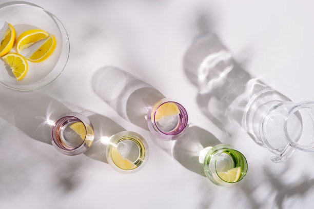 彩色的玻璃杯，清新的水和一片柑橘在盘子上的白色背景。夏天的创意平面躺着坚硬的阴影。图片下载