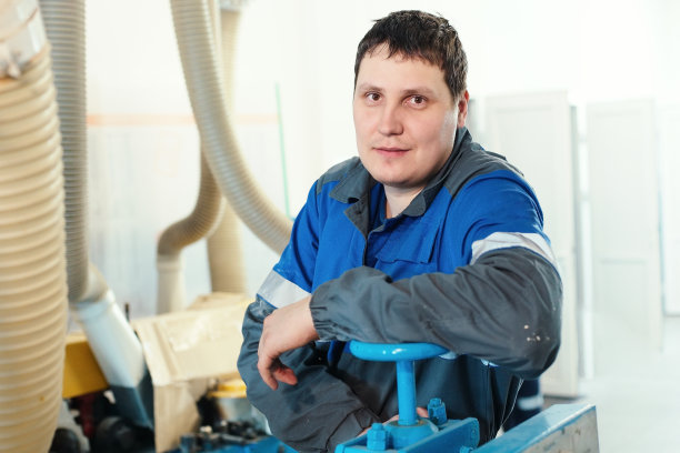 一个年轻工人的肖像在工作场所的机器上穿着工装裤。图片下载