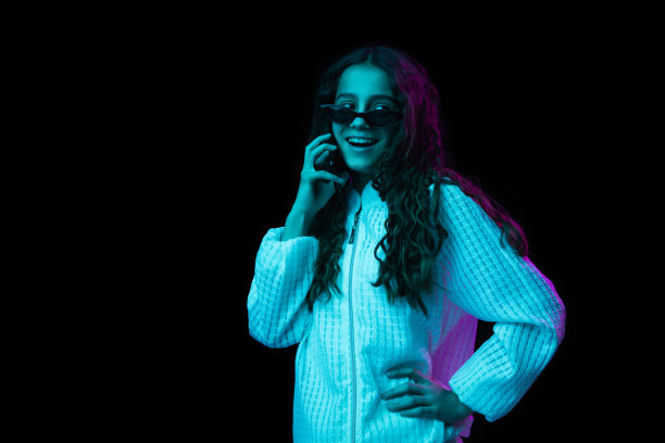 年轻美丽的女孩讲电话孤立在黑暗背景霓虹灯图片下载