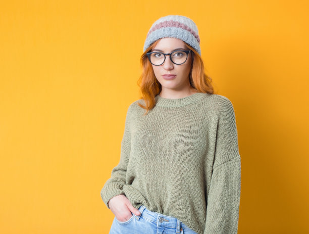 美丽的女人双手插在口袋里看着相机，而站在黄色背景孤立。有吸引力的女孩图片下载