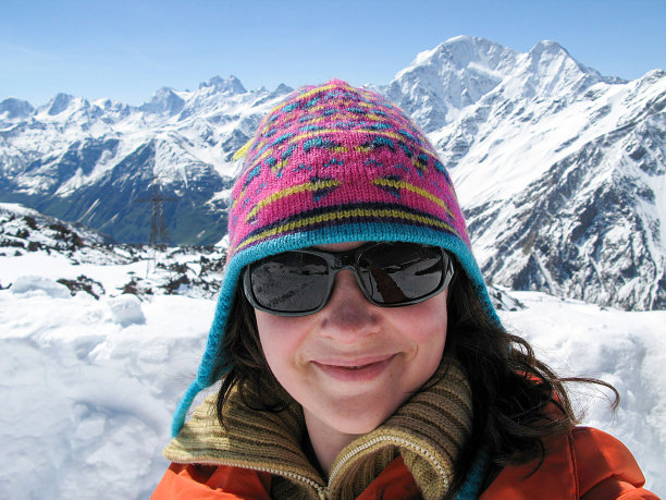 一名年轻的白人女子站在一座白雪皑皑的山顶上看着摄像机。图片下载