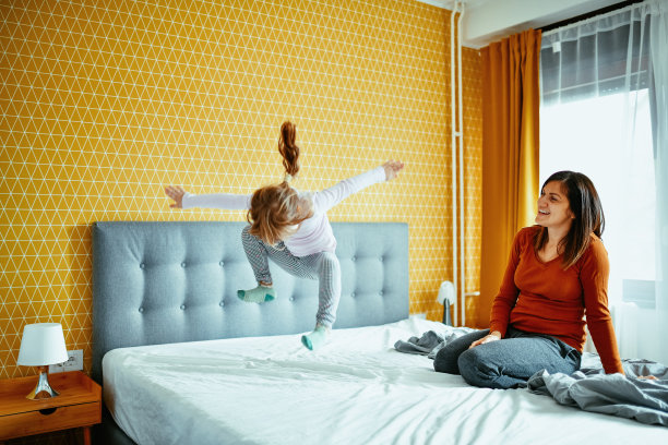 妈妈和女儿在卧室里玩，女孩在床上跳图片下载