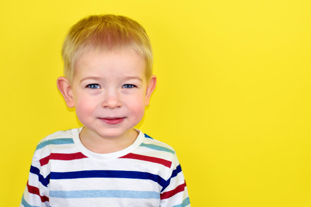 彩色背景上的快乐微笑的小男孩。黄色背景上的美丽的两岁欧洲男孩的肖像。为文本复制空间。图片下载