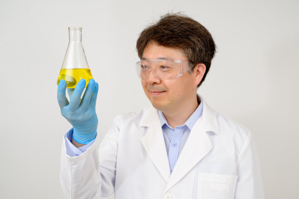 一位中年亚洲男性科学家的肖像穿着白色的实验室长袍和手套，手里拿着一个实验容器。图片下载