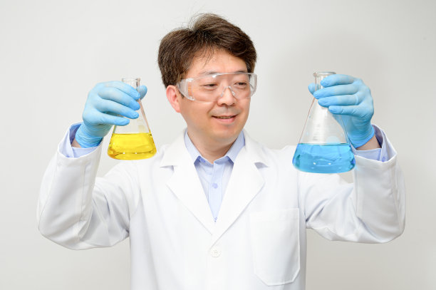 一位中年亚洲男性科学家的肖像穿着白色的实验室长袍和手套，手里拿着一个实验容器。图片下载