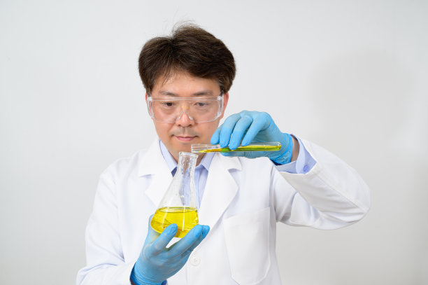 一位中年亚洲男性科学家的肖像穿着白色的实验室长袍和手套，手里拿着一个实验容器。图片下载