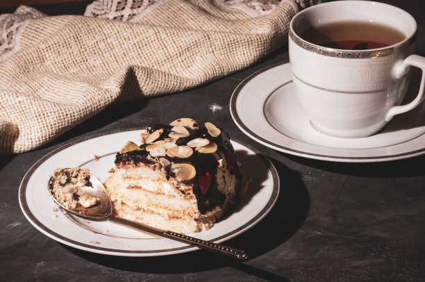 静物层次的自制海绵蛋糕和一杯红茶在一个白色的盘子，和亚麻餐巾，黑色的背景，强光，照片在一个低的关键。图片下载