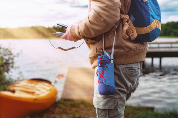 游客手持移动充电器，手持智能手机。一个背着背包的男人在一个皮艇和森林的背景下旅行。图片下载