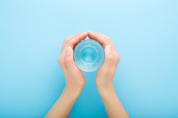 年轻的成年妇女手捧一杯淡水在浅蓝色的桌子背景。柔和的颜色。特写镜头。视角拍摄。健康饮料的概念。自顶向下的观点。图片下载