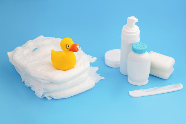 婴儿洗澡。可爱的小黄鸭坐在尿布堆上。奶油、乳液和肥皂。粉末、棉毛和梳子图片下载