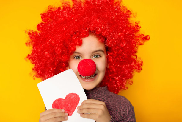 四月一日愚人节的概念。情人节快乐。鲜红的丘比特在情人节。有趣的女孩小孩小丑玩金色1和4气球孤立黄色背景。图片下载