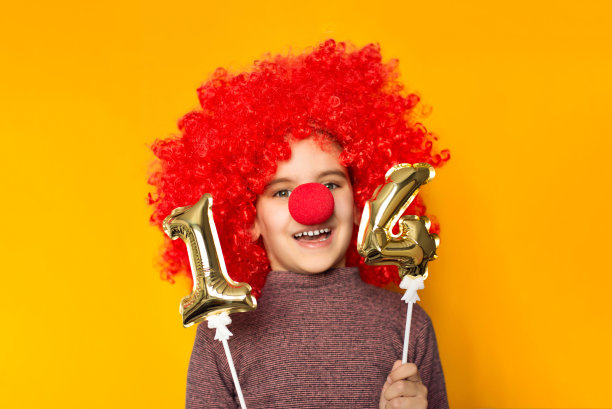 四月一日愚人节的概念。情人节快乐。鲜红的丘比特在情人节。有趣的女孩小孩小丑玩金色1和4气球孤立黄色背景。图片下载