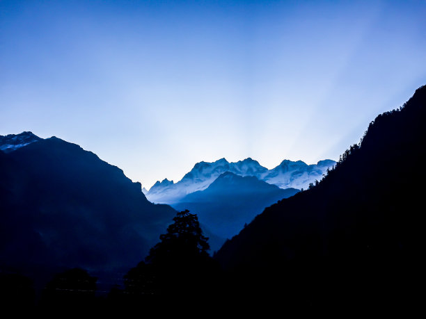 群山剪影在蓝天的背景上，阳光在群山中图片下载