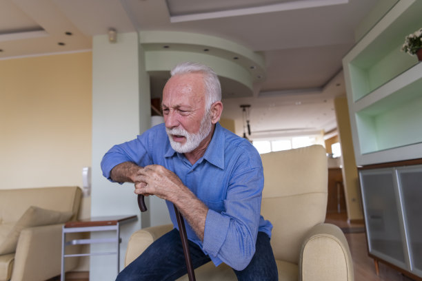 一位拄着拐杖的残疾老人坐在家里，背部疼痛难忍，试图站起来。图片下载