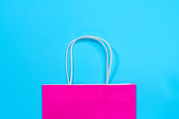 一半的酸性粉色环保购物纸袋，手柄由可回收材料制成，用于包装和携带货物，蓝色背景，俯视图，复印空间图片下载