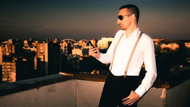 英俊的男人戴着太阳镜享受城市的天际线，同时发短信打电话图片下载