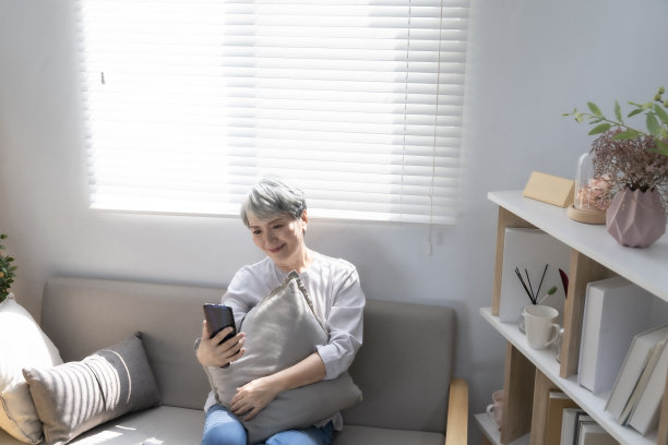 躺在客厅沙发上用智能手机与孙子进行视频会议的老年妇女。享受时光的生活方式家庭在家里的概念。看着相机的人像图片下载