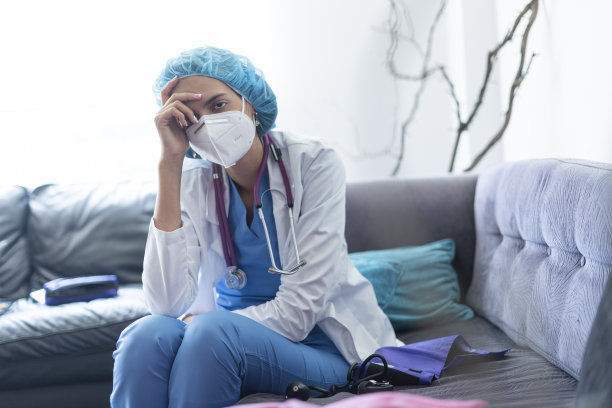 这是一幅医生在病人家里的沙发上睡着的照片，她穿着制服，戴着抗击COVID - 19的口罩，多次家访导致极度疲劳图片下载