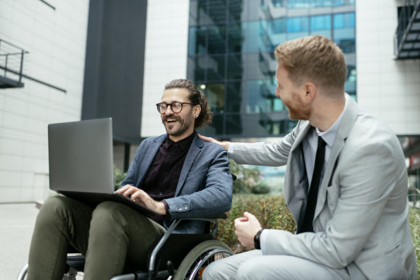 一个坐着轮椅的商人和一个休息的同事。库存图片图片下载