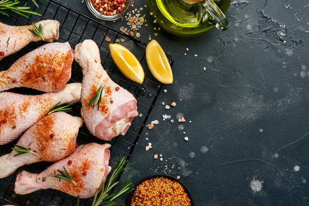 生鸡腿和烹饪材料在黑色的石头背景。食物背景，生肉与香料在黑色的桌子。前视图。图片下载