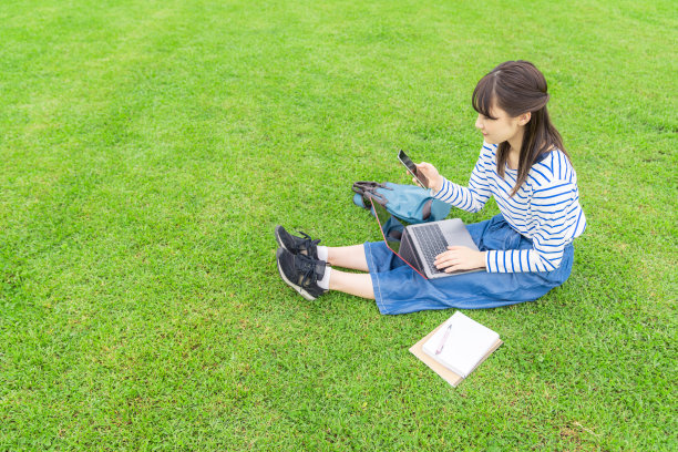 亚洲女学生在草地上使用笔记本电脑。图片下载