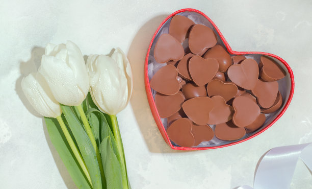 女人礼物的概念。白色的背景上点缀着郁金香和巧克力糖果。图片下载