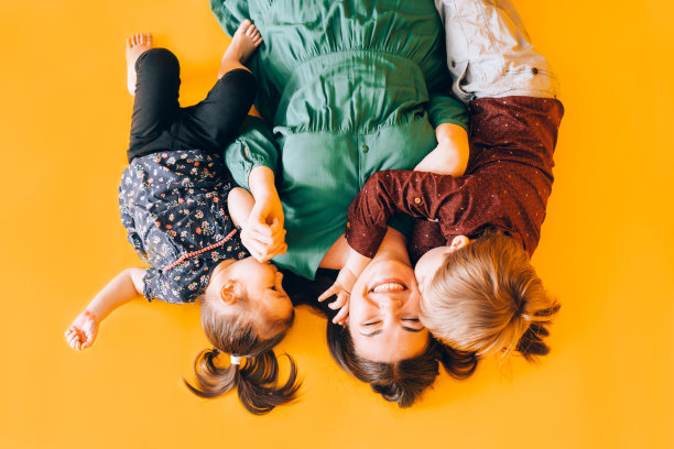 快乐的妈妈带着孩子躺在黄色的背景上。花时间和孩子在一起图片下载