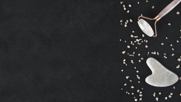 家用水疗沙龙，水粉刮刀和面部按摩辊。皮肤护理趋势。提升健康年轻肌肤。有机化妆品在黑暗的背景与粉红色海盐。副本的空间。前视图。图片下载