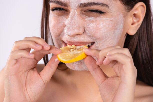 放大照片的黑发女子与保湿面膜咬一片柠檬。脸上戴着奶油柑橘面膜的女孩。美容护肤理念。图片下载