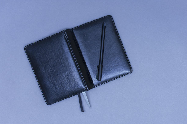 桌上放着一架打开的黑色皮革滑翔机，上面放着一支笔作笔记。图片下载